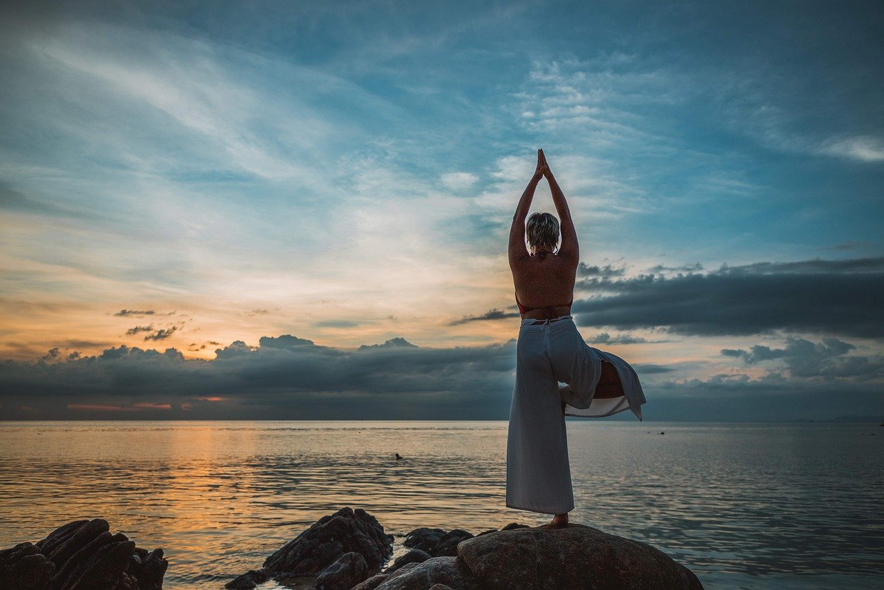 photo of woman doing yoga on rock by the sea